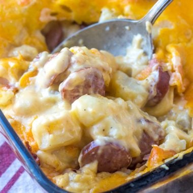 a silver spoon digging into a baking dish filled with cheesy potato and smoked sausage casserole