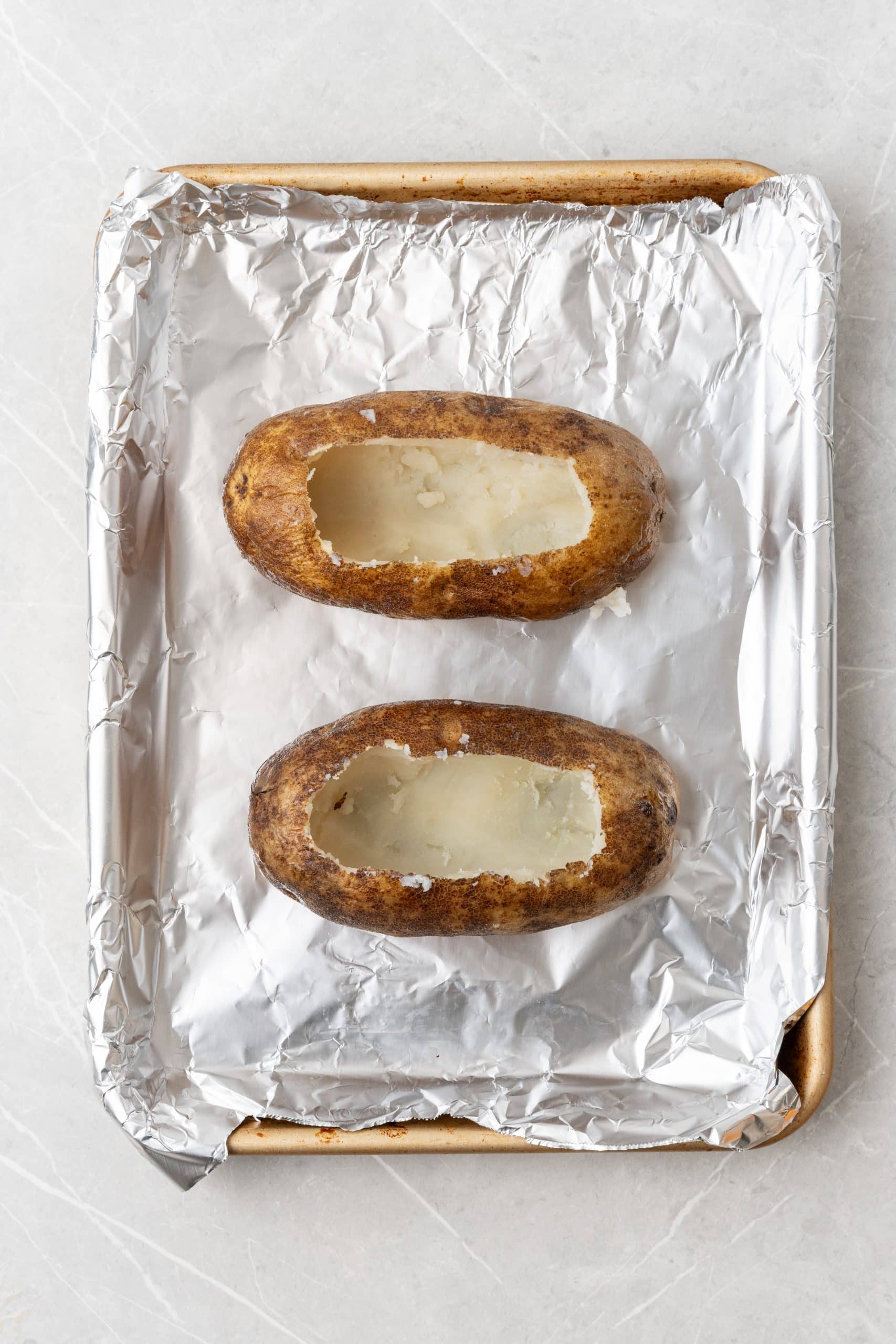two hollowed out baked potatoes on a foil lined baking sheet