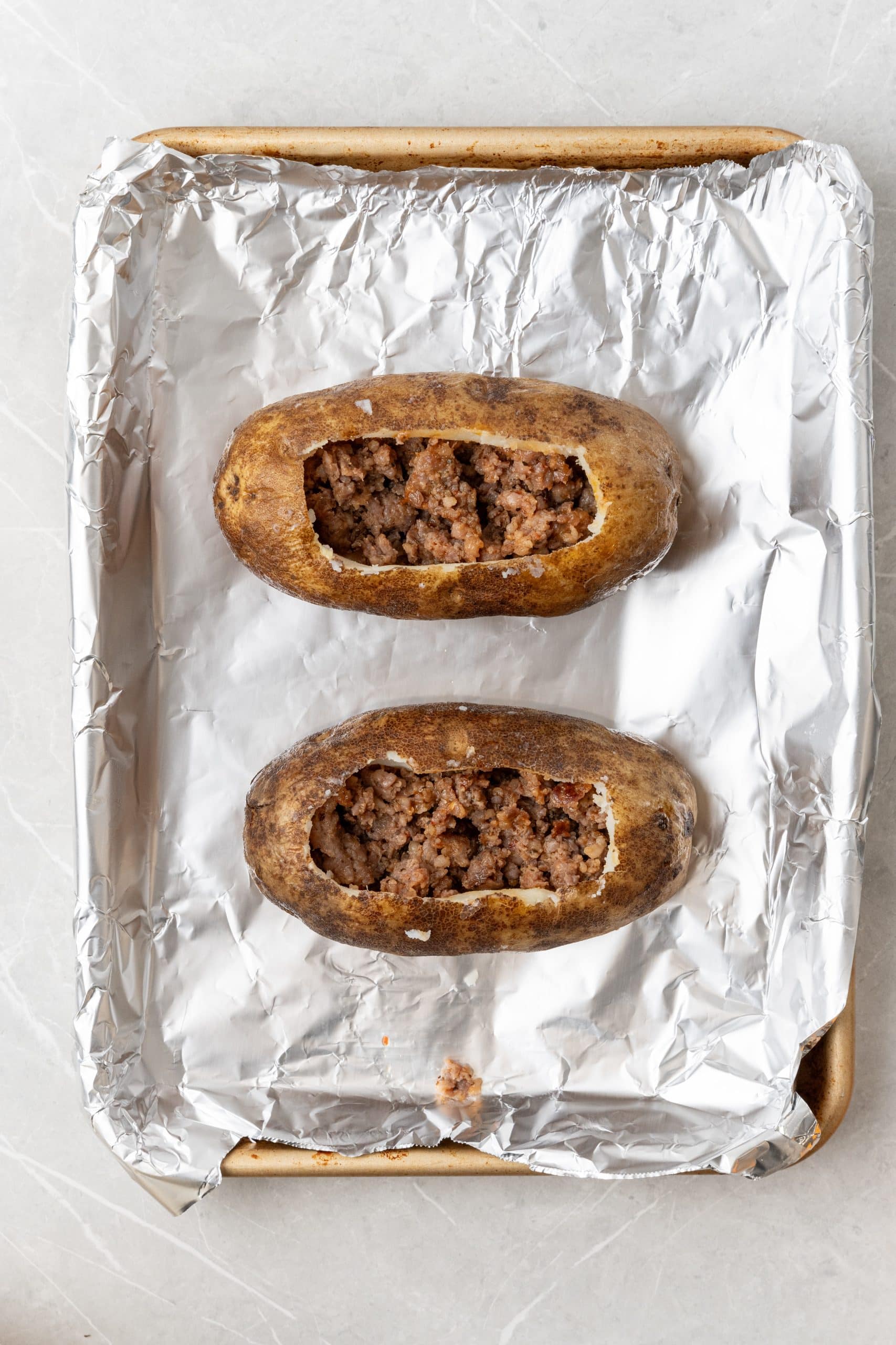 sausage filled hollowed out baked potatoes on a foil lined baking sheet