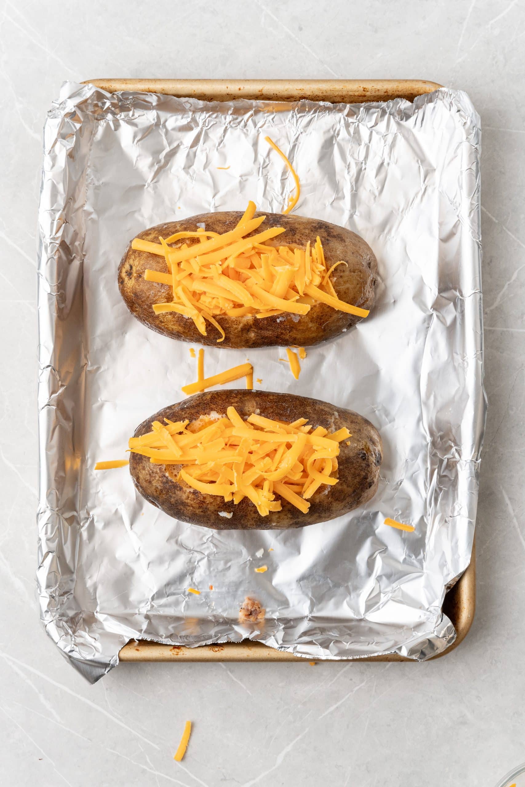 shredded cheese topped breakfast baked potatoes on a foil lined baking sheet