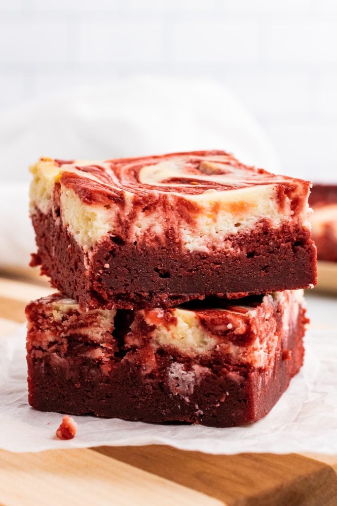 two red velvet cheesecake brownies stacked on top of a white piece of parchment paper