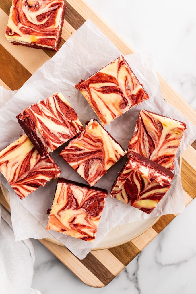 red velvet cheesecake brownie squares in a pile on a parchment paper covered cutting board