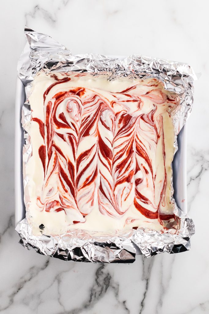 swirled ribbons of red velvet cheesecake brownie batter in an aluminum foil lined baking dish