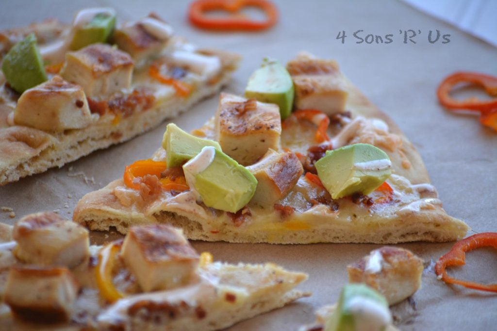 A slice of crispy toasted naan bread is shown topped with chicken, sweet pepper rings, avocado and cheese