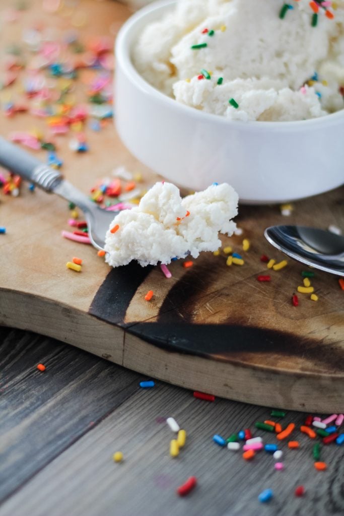 a silver spoon topped with snow ice cream and surrounded by rainbow sprinkles on a wooden cutting board
