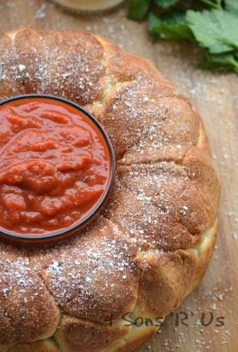 pepperoni pizza pull apart bread with a small glass bowl filled with marinara sauce in the center on a wooden cutting board