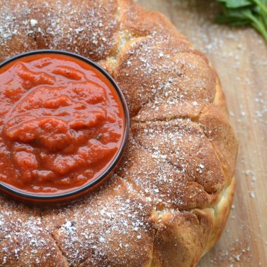 pepperoni pizza pull apart bread with a small glass bowl filled with marinara sauce in the center on a wooden cutting board