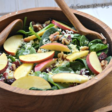 spinach salad topped with nuts, sliced apples, and berries in a large wooden serving bowl