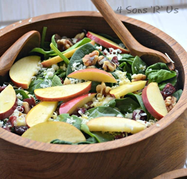 spinach salad topped with nuts, sliced apples, and berries in a large wooden serving bowl