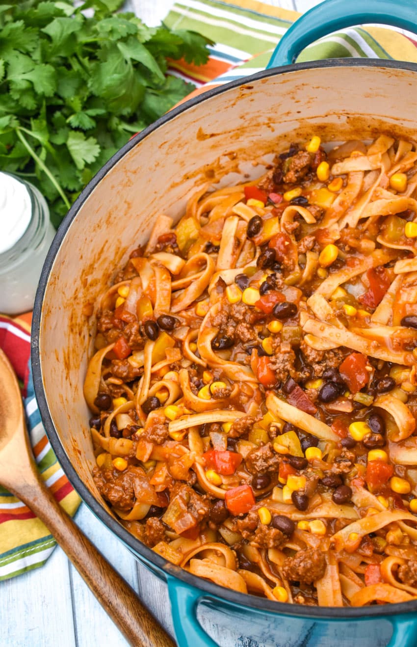 one pot taco spaghetti in a large dutch oven with fresh herbs and a wooden spoon on the side