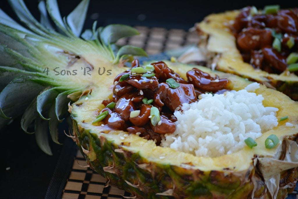 Chicken Teriyaki Pineapple Boats shows saucey, teriyaki glazed chicken pieces served next to tender white rice in a halved, hollowed out pineapple bowl