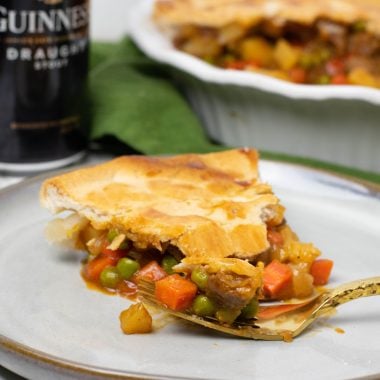 a slice of steak and guinness pie on a gray ceramic plate with a gold fork