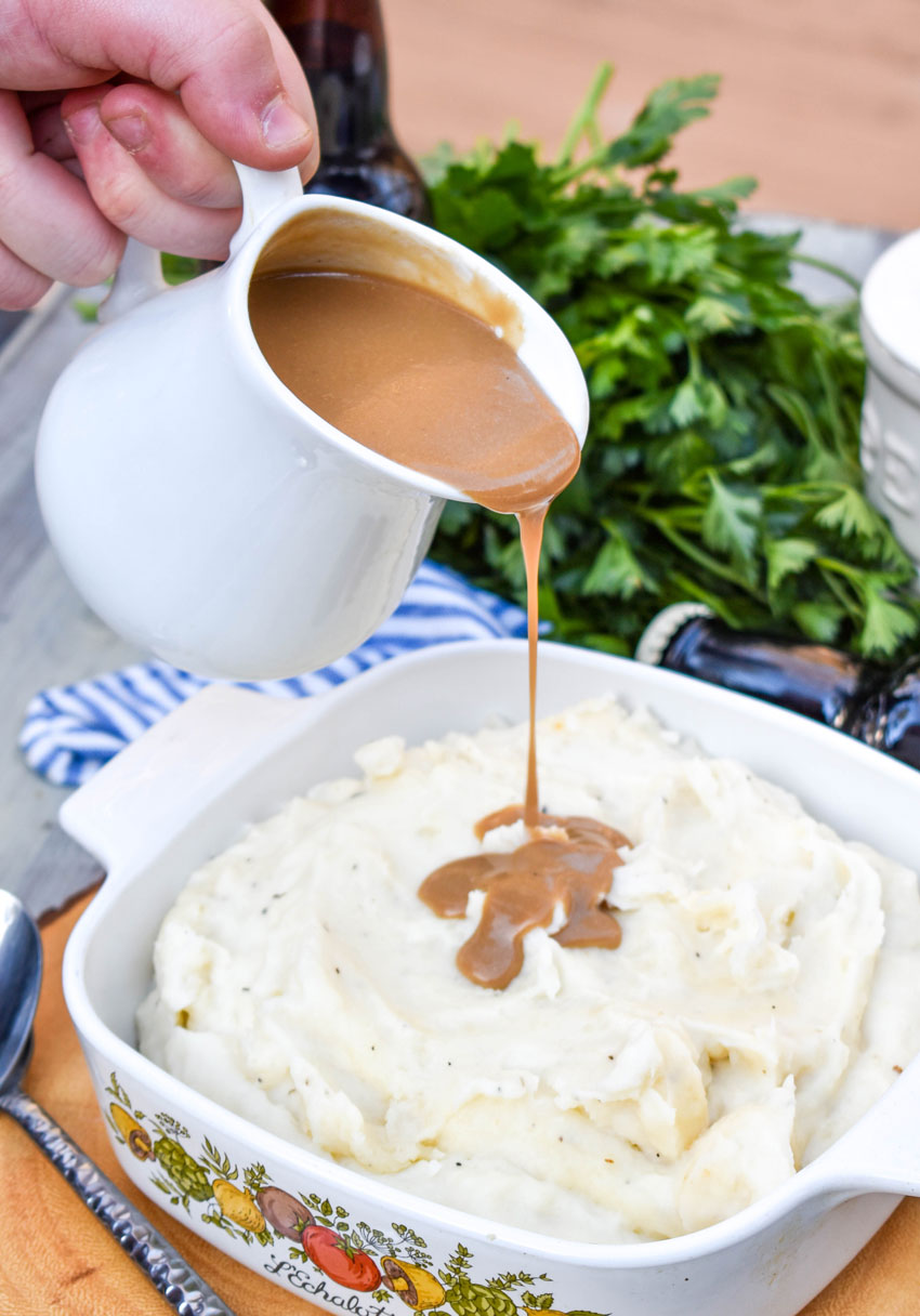 dijon stout gravy being poured over a bowl of whipped mashed potatoes