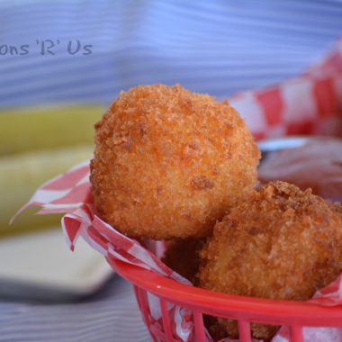 giant cheesy tater tots served in a red, paper lined lunch basket with dill pickle spears in the background
