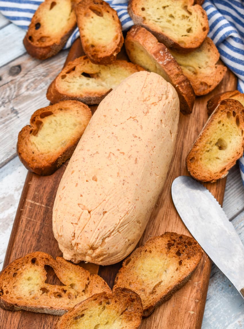 a block of homemade sriracha honey butter on a wooden cutting board surrounded by toasted baguette slices