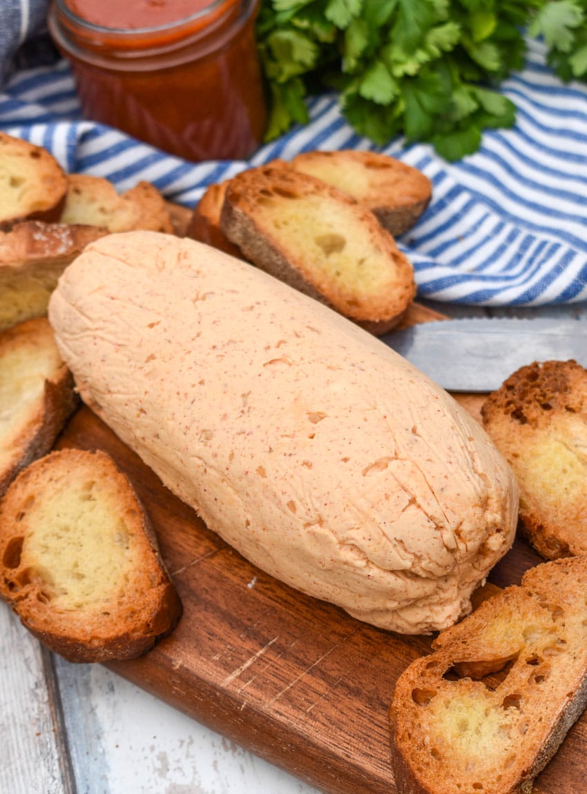 a bloack of homemade sriracha honey butter on a wooden cutting board surrounded by toasted baguette slices