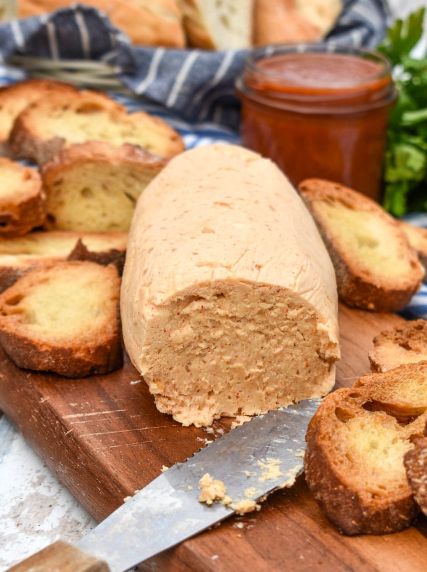 a block of homemade sriracha honey butter on a wooden cutting board surrounded by toasted baguette slices