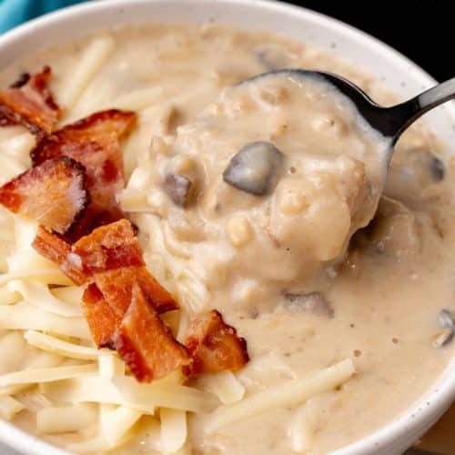 a black spoon scooping creamy swiss mushroom potato soup out of a white bowl