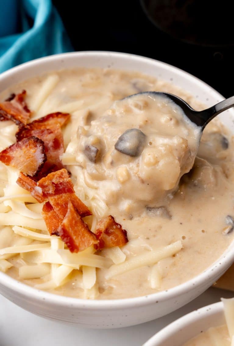 a black spoon scooping creamy swiss mushroom potato soup out of a white bowl