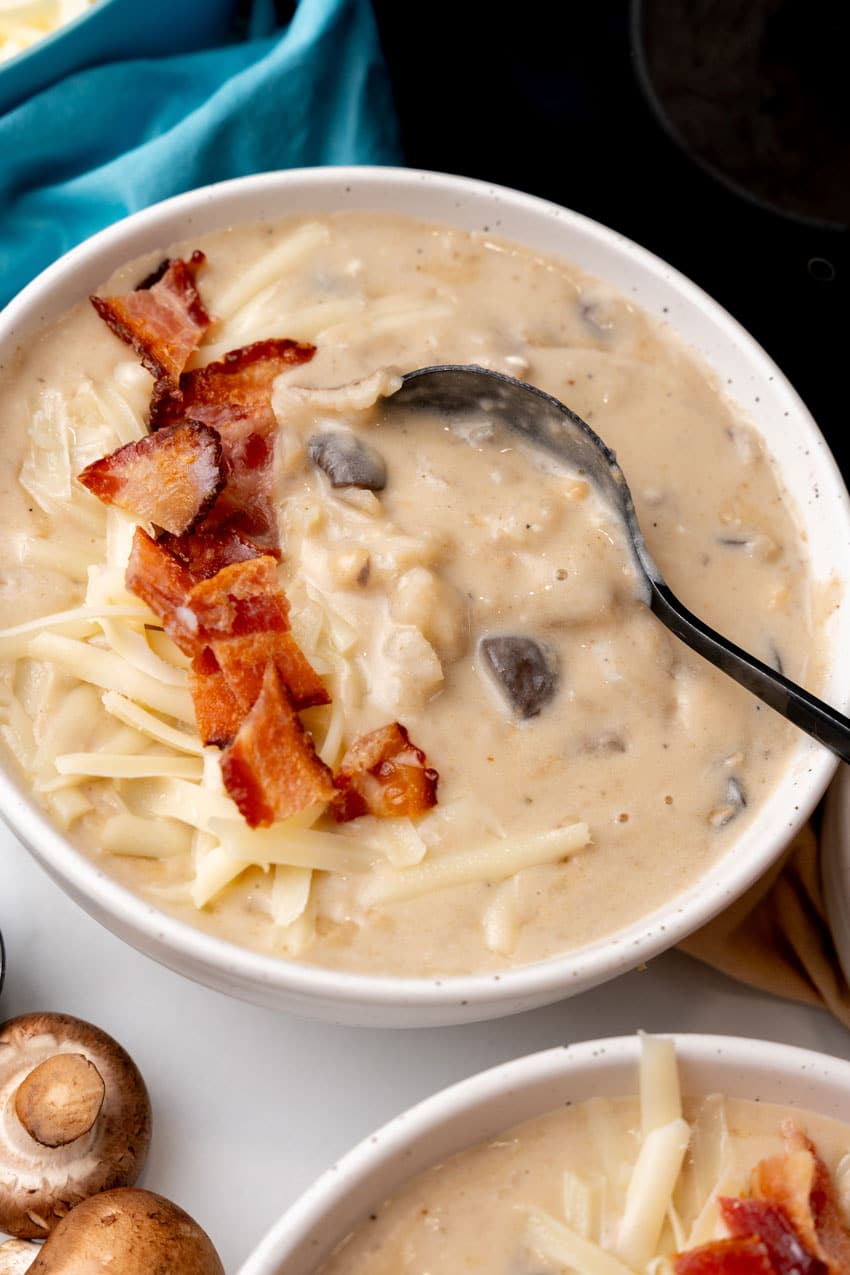 a black spoon scooping creamy swiss mushroom potato soup out of a white bowl