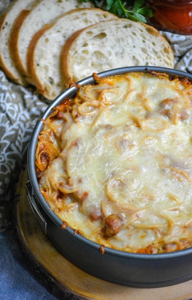 baked spaghetti pie shown in a springform pan after baking with sliced bread for serving