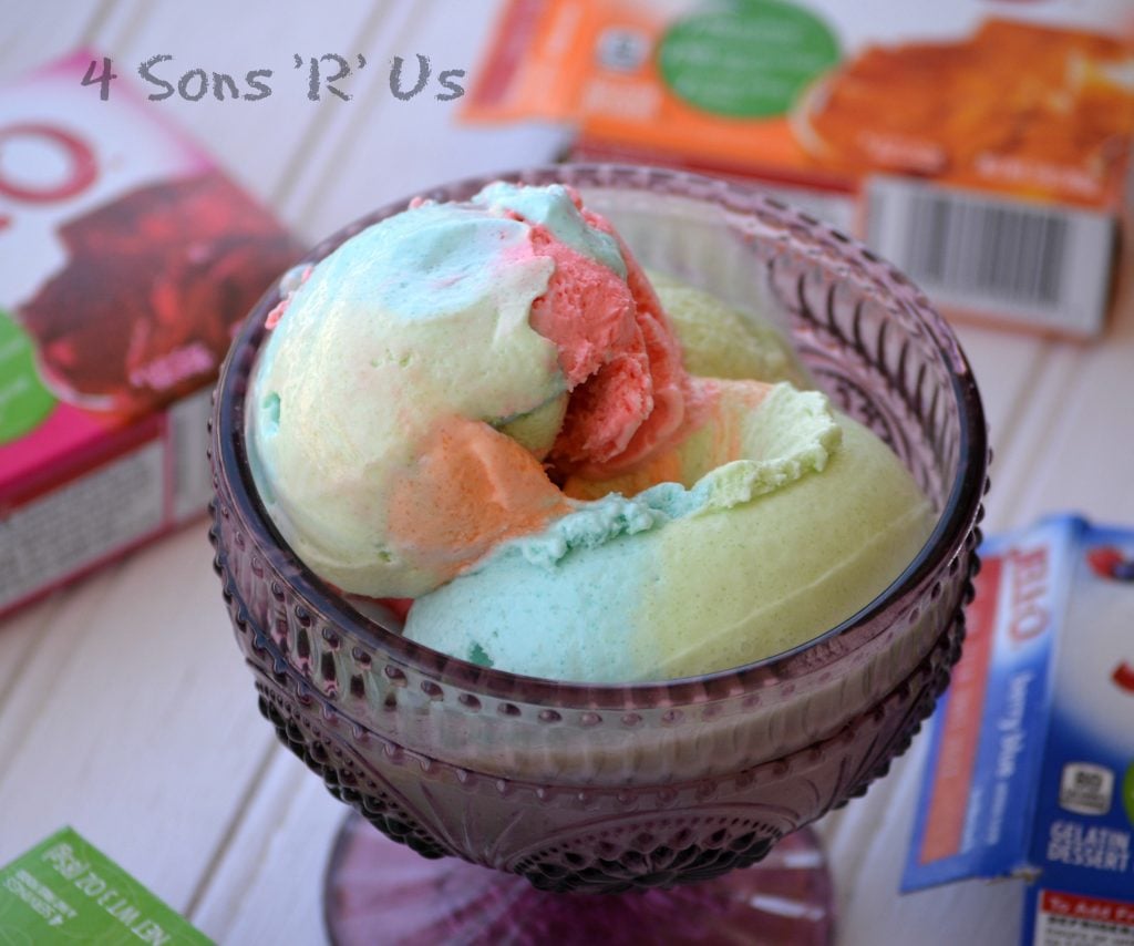 Jello Rainbow Sherbet Ice Cream scooped into a purple glass bowl with a variety of flavors of jello boxes in the background