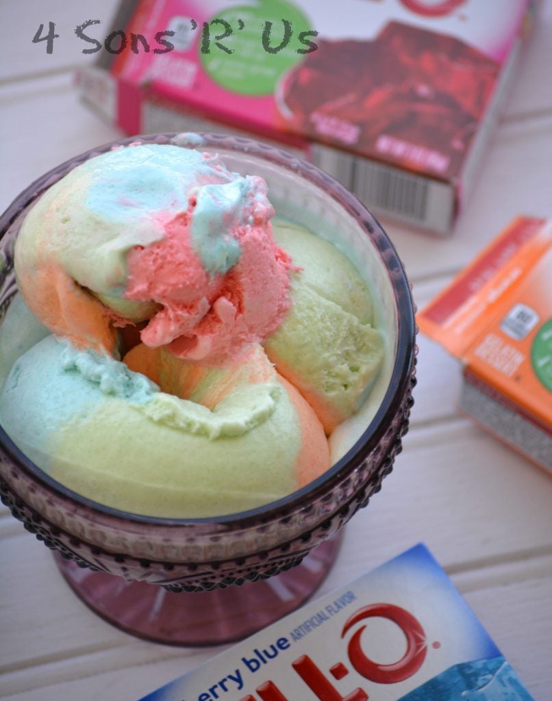 Jello Rainbow Sherbet Ice Cream scooped into a purple glass bowl with a variety of flavors of jello boxes in the background