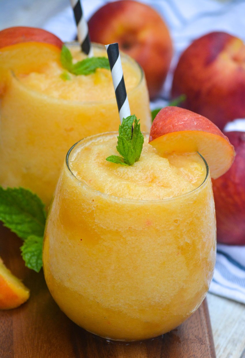 peach white wine slushies in stemless win glasses garnished with fresh sliced of fruit and mint leaves