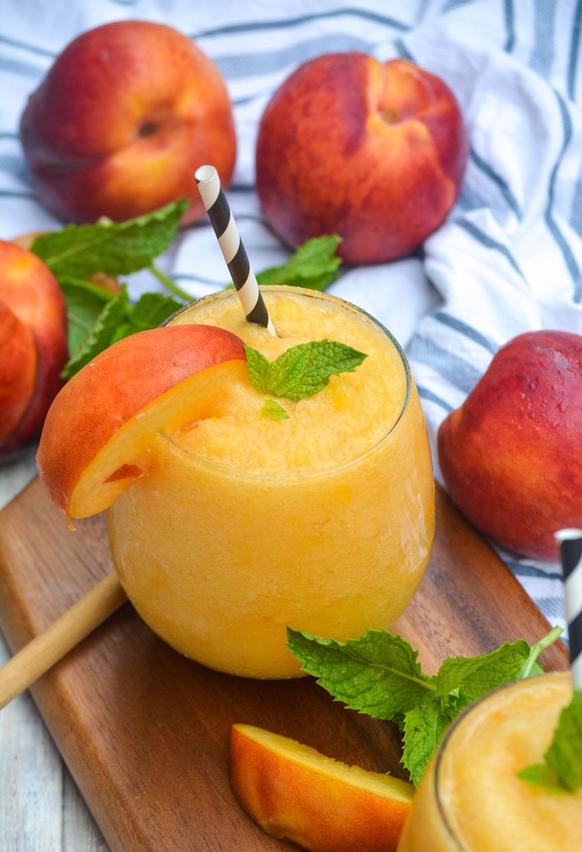 peach white wine slushies on a wooden cutting board with fresh peaches and mint leaves