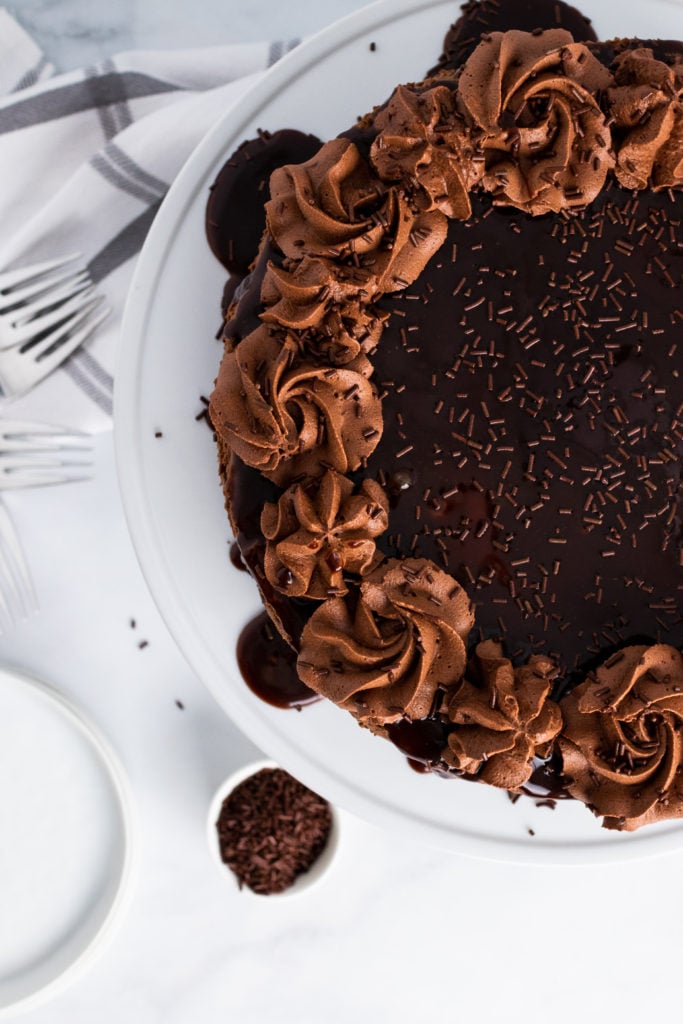 hot fudge brownie cheesecake garnished with chocolate sauce and chocolate whipped cream swirls on a white cake pedestal