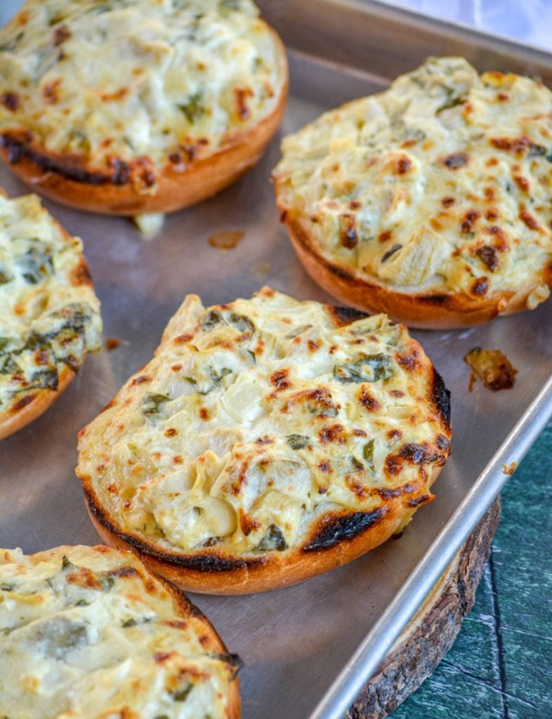 toasted Spinach & Artichoke Bagel Melts shown on a metal sheet pan