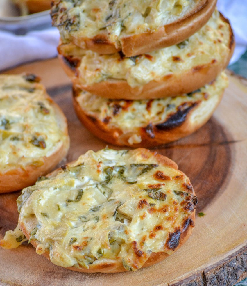 Spinach & Artichoke Bagel Melts shown on a wooden log cutting board