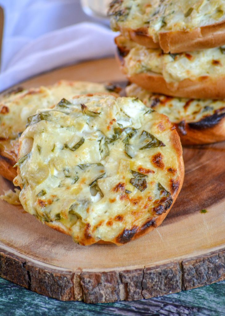 Spinach & Artichoke Bagel Melts shown on a wooden cutting board