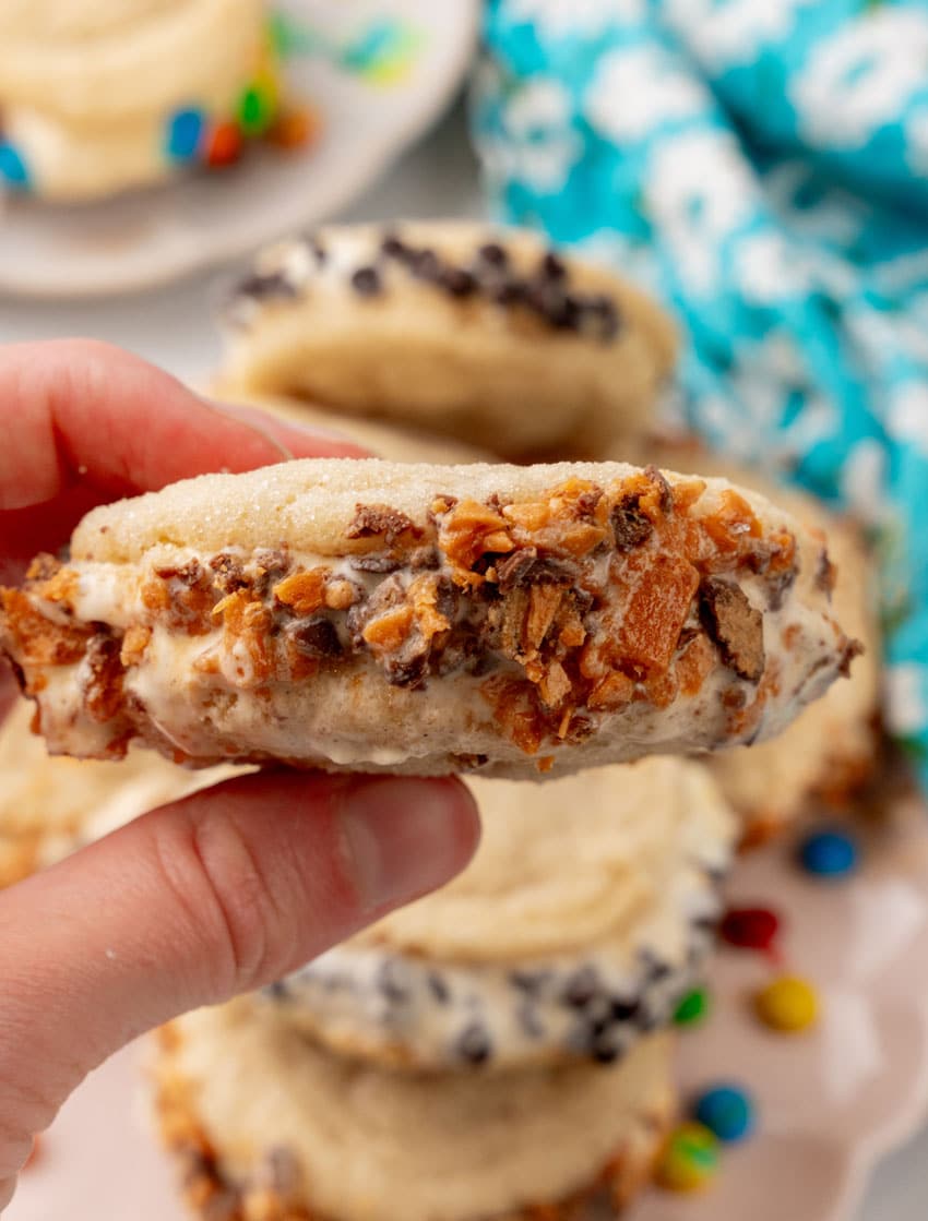 a hand holding up a homemade butterfinger sugar cookie ice cream sandwich