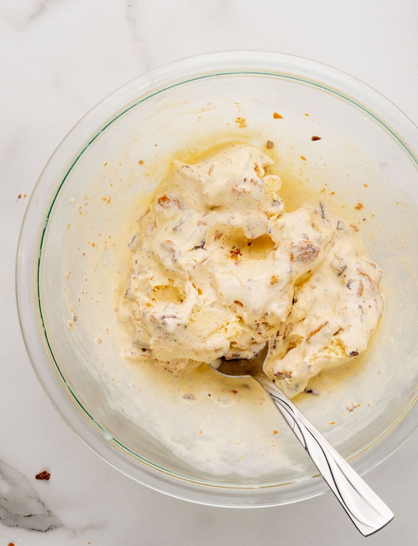 butterfinger candy pieces mixed with softened vanilla ice cream in a glass mixing bowl