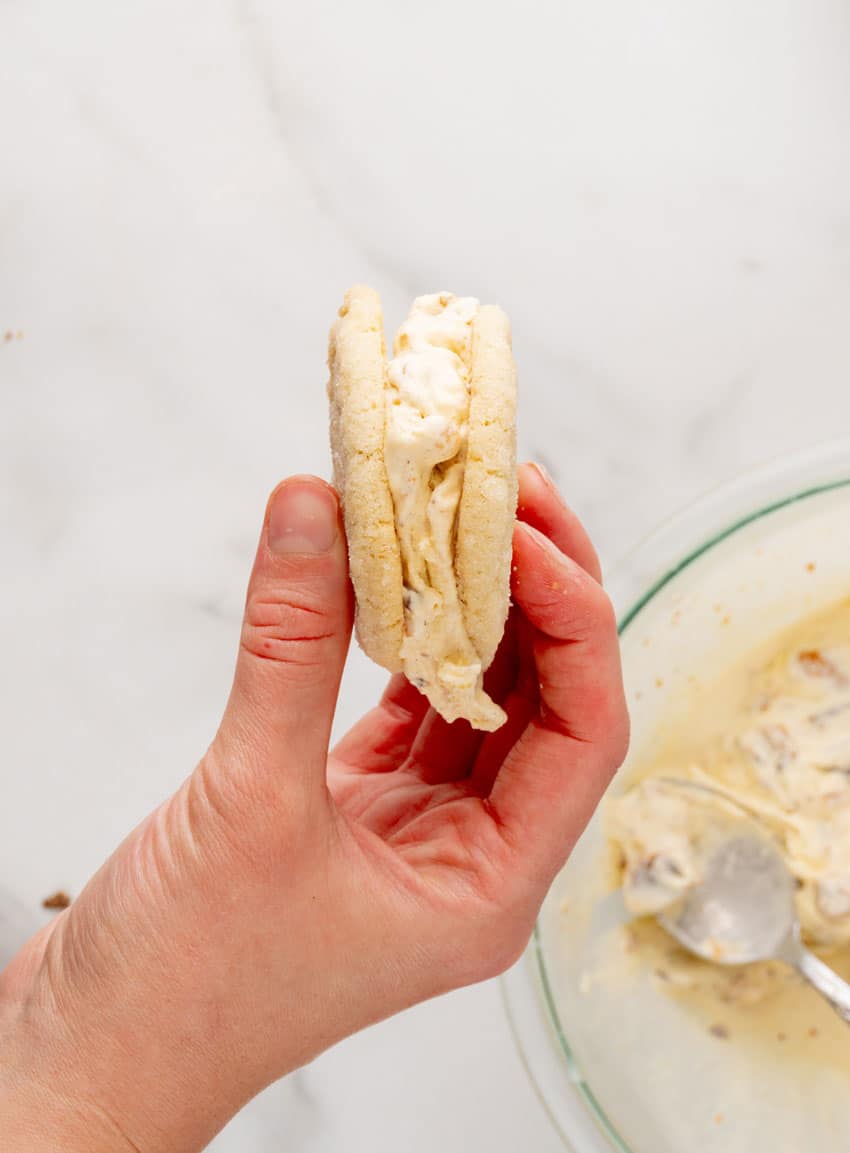 a hand holding up a homemade vanilla sugar cookie ice cream sandwich