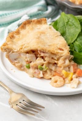 a slice of seafood pot pie next to leafy greens on a white dinner plate