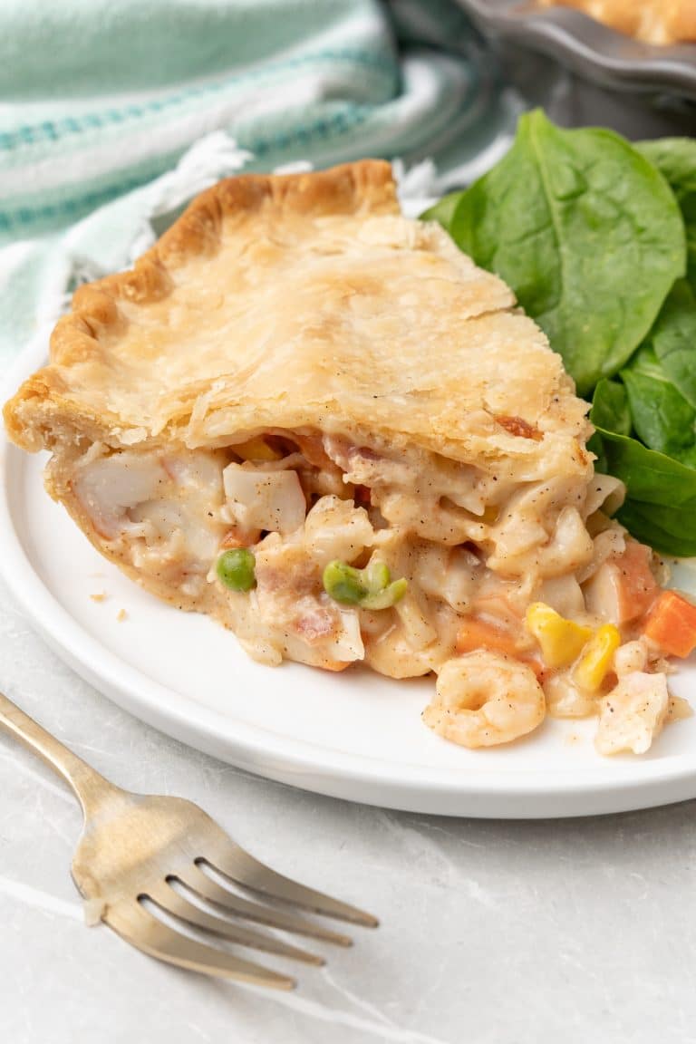 a slice of seafood pot pie next to leafy greens on a white dinner plate