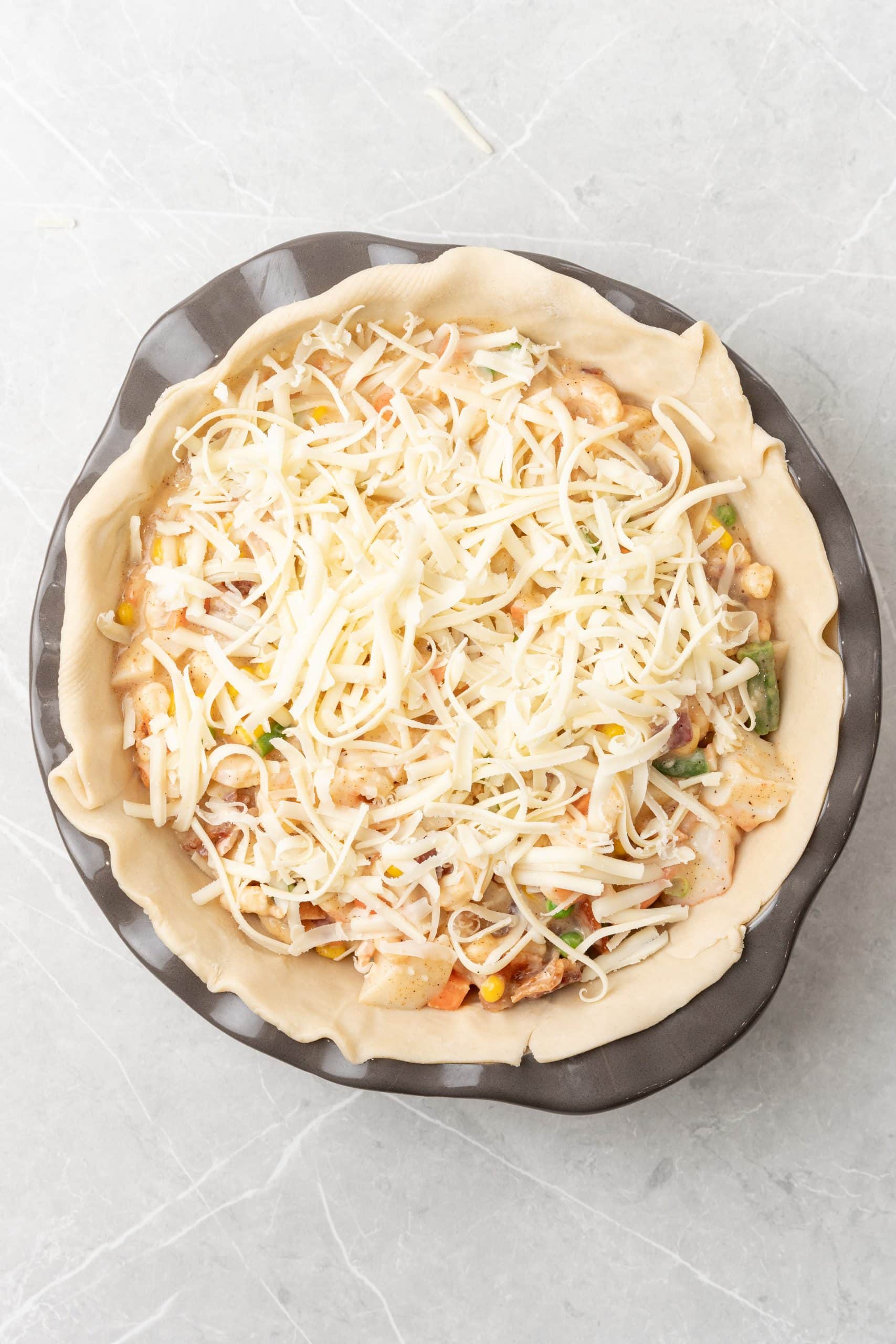 shredded cheese topped seafood pot pie filling in an unbaked pie crust in a metal pie pan