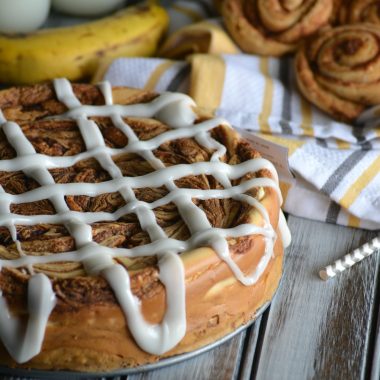 cream cheese glaze drizzled across a cinnamon bun cheesecake with ripe bananas in the background