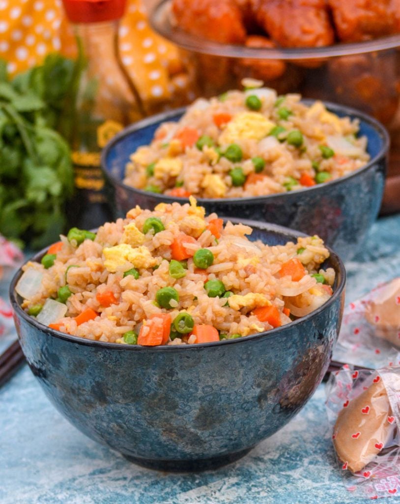 Panda Express copy cat fried rice shown served in two black bowls with fortune cookies and orange chicken in the background