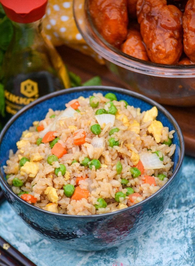 a bowl shown full of this copy cat fried rice with a bottle of soy sauce and a bowl of orange chicken in the background