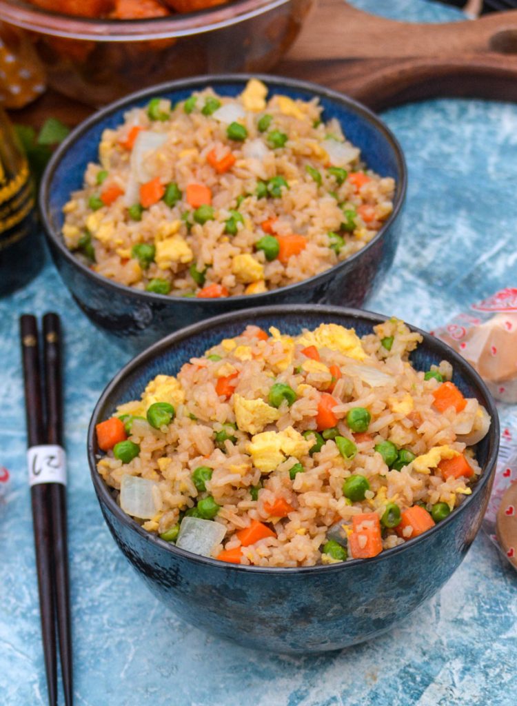 Panda Express copy cat fried rice shown served in two black bowls with fortune cookies and orange chicken in the background