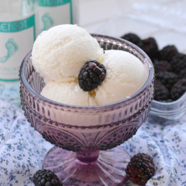 three scoops of dessert wine ice cream in a purple bowl with a fresh blackberry on top