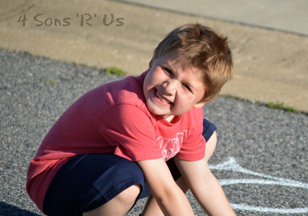 a boy drawing with homemade sidewalk chalk on an asphalt street