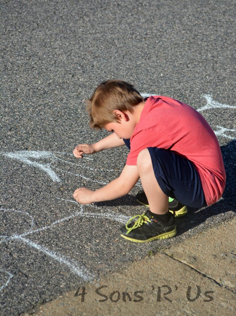 a boy drawing with homemade sidewalk chalk on an asphalt street