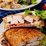 two halves of a chipotle chicken bacon ranch panini on a white plate with leafy greens on the side