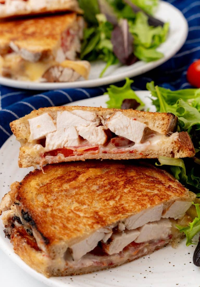 two halves of a chipotle chicken bacon ranch panini on a white plate with leafy greens on the side