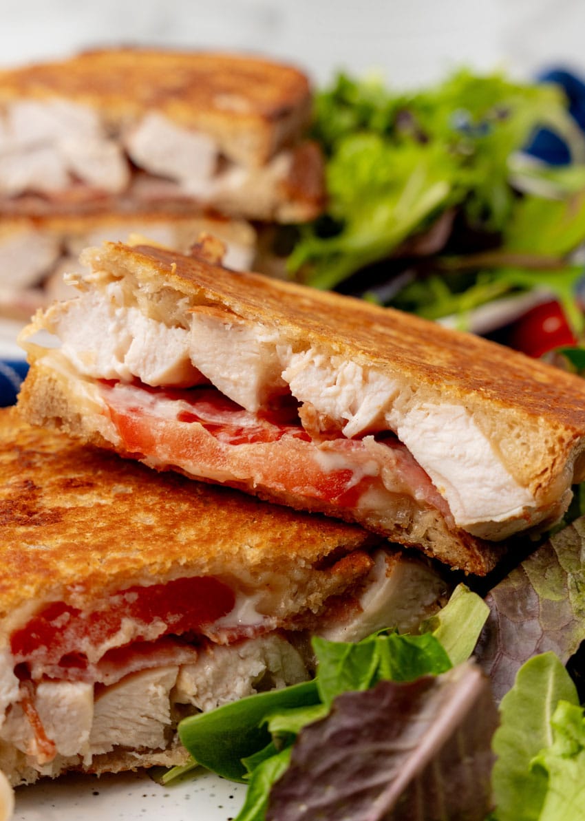 two halves of a chipotle chicken bacon ranch panini on a white plate with leafy greens on the side