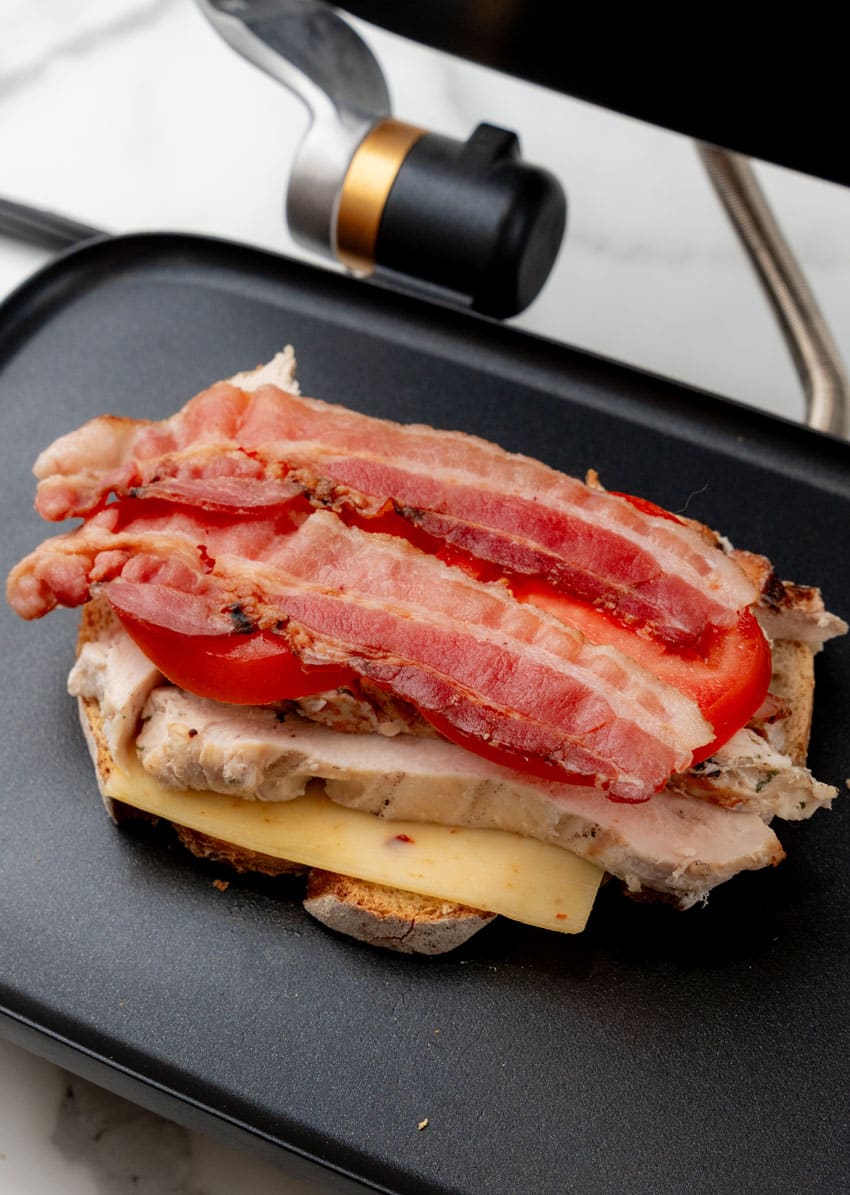 crispy bacon and strips of grilled chicken on a thick slice of bread on a panini grill